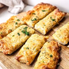 several pieces of bread on a cutting board with parmesan cheese and green herbs