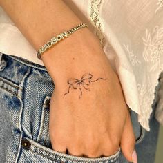 a woman's hand with a small bow tattoo on her left wrist and the word love written in cursive writing