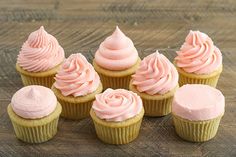 several cupcakes with pink frosting sitting on a wooden table