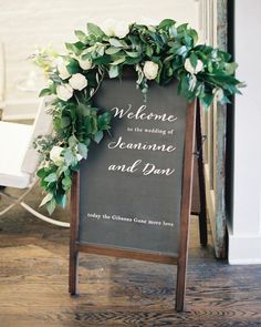 the welcome sign is decorated with greenery and white flowers for an elegant touch to the ceremony