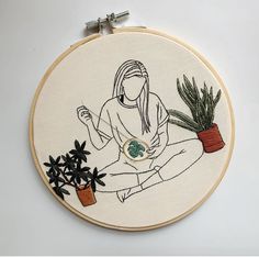 a woman is sitting on the ground next to some plants and holding a potted plant