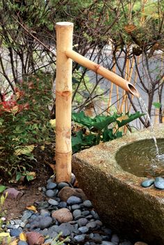 a water fountain made out of bamboo sticks and rocks in a garden with trees behind it