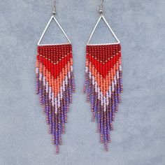 a pair of earrings with red, purple and white beads hanging from it's sides