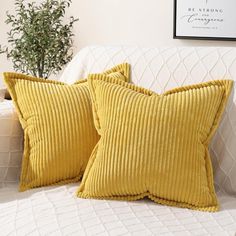 two yellow pillows sitting on top of a white couch next to a potted plant