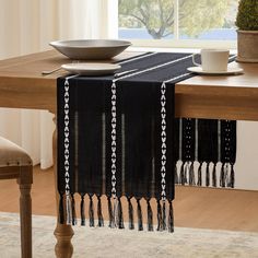 a black table runner with white tassels on it in front of a window