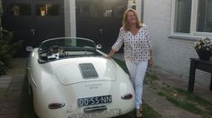 a woman standing next to a white sports car in front of a house with two windows