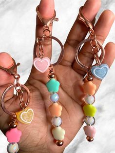 a person holding three different key chains in their hand with hearts and other charms attached to them