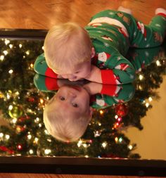 two toddlers in matching christmas pajamas looking at each other's reflection on a mirror