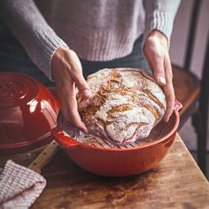 a person holding a loaf of bread in a red bowl on top of a wooden table