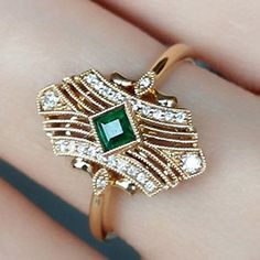 a close up of a person's hand wearing a ring with an emerald and white diamond