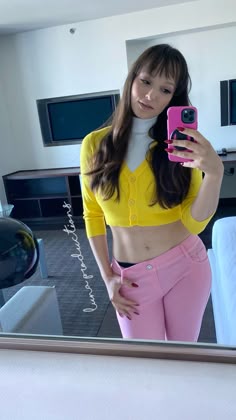 a woman taking a selfie in front of a mirror wearing pink pants and a yellow crop top