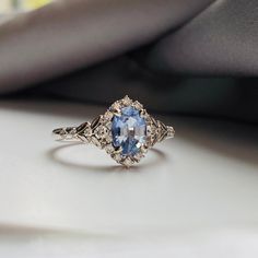 an oval shaped blue and white diamond ring on top of a cushioned surface with grey fabric in the background