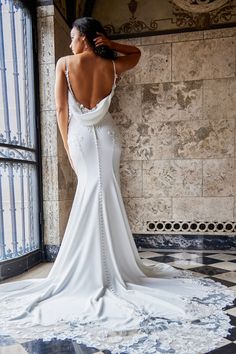 a woman in a white dress is standing near a wall and looking out the window