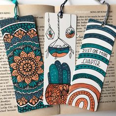 three bookmarks with designs on them are hanging from the pages of an open book