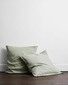 two green pillows sitting on top of a wooden floor next to a white painted wall