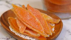 sliced orange peels on a wooden plate next to a jar of sugary liquid