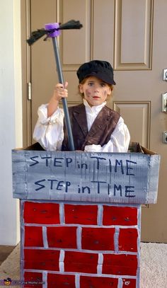 a young boy dressed as a chimney sweeper holding a broom and standing in front of a brick wall