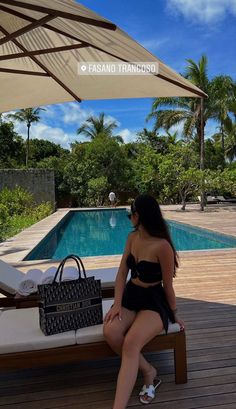 a woman sitting on a bench next to a pool with an umbrella over her head