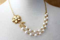 A beautiful gold plated  flower  is set with a pearl , set on a filagree and attached to a gold plated leaf trailed by a two strands of hand wired linked off white Swarovski glass pearls of 8 mm. The necklace is finished with gold plated cable chain, necklace measures 16 .5" long. Lobster clasp. H A N D M A D E  * We hand make all pieces in our Water Mill New York studio * We source eco friendly packaging and materials, including recyclable mailers! FREE BOX AND WRAP ON EVERY ORDER P R O D U C T I O N ∙ T I M E S All items are made to order, our average production time is 1-3 business days but can take up to 5 sometimes. If you need it sooner, please leave a message in the "note to seller" so we can try to speed things up for you! E X P E D I T E D ∙ O P T I O N S Each drop down menu has e Gold Flower-shaped Jewelry For Wedding, Gold Flower Shaped Jewelry For Wedding, Delicate Gold Pearl Bridal Necklace, Delicate Gold Bridal Necklace With Pearls, Classic Gold Bridal Necklace For Wedding, Gold Pearl Flower Jewelry, Gold Pearl Chain Necklace For Mother Of The Bride, Delicate Gold Bridal Necklace For Anniversary, Dainty Gold Bridal Necklace For Wedding