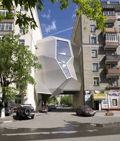 an unusual building in the middle of a city with cars parked on the street below it