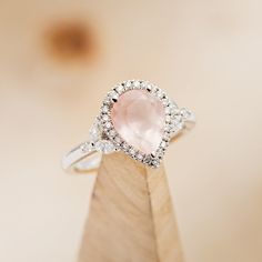 a pink diamond ring sitting on top of a wooden stand