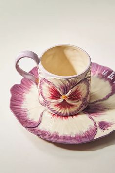 a coffee cup and saucer sitting on top of a white plate with purple flowers