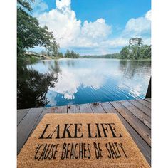 a door mat that says lake life cause beaches be salty on a wooden dock next to a body of water