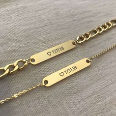 two personalized gold chain bracelets with names on them, sitting on a gray fabric