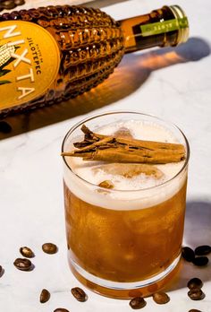 a glass filled with ice and cinnamon on top of a table next to coffee beans