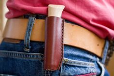 a person wearing jeans with a brown leather belt and a red t - shirt behind their back pocket