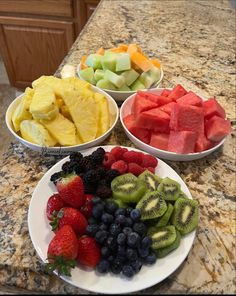 four bowls filled with different types of fruit on top of a marble countertop in a kitchen