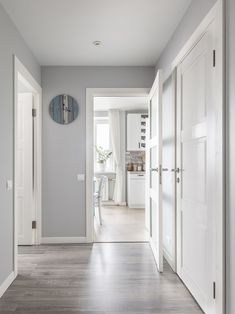 an empty hallway leading to a kitchen and dining room with gray walls, wood flooring and white trim