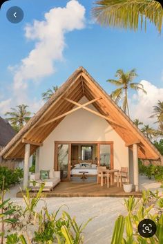 a small white house with a thatched roof on the beach near palm trees and blue sky