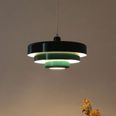 a black, green and white light hanging from a ceiling over a vase with flowers