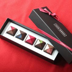 three chocolates in a black box on a red cloth with a pink ribbon around it