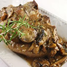 a white plate topped with meat covered in mushroom gravy and garnished with fresh herbs