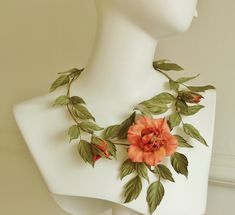 a white mannequin with an orange flower and green leaves on it's neck