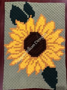 a crocheted sunflower is shown on a gray and yellow blanket with black centers