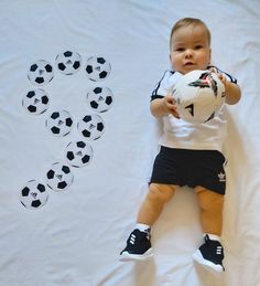 a baby holding a soccer ball in front of a heart made out of soccer balls