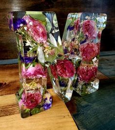 two clear vases with flowers on them sitting on a wooden table next to each other