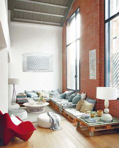 a living room filled with lots of furniture next to a large window and brick wall