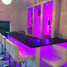 the bar is lit up with purple lights and white barstools in front of it