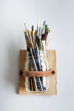 a mason jar filled with paint brushes on top of a wooden shelf next to a white wall