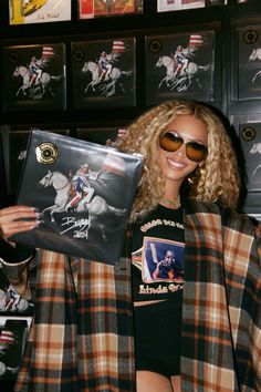 a woman in plaid jacket and sunglasses holding up a vinyl album with horse images on it