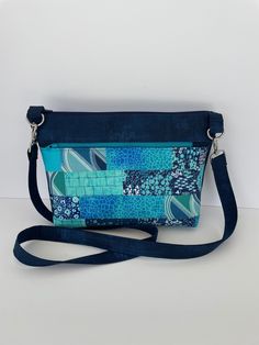 "The popular \"Sarasota\" shoulder bag features a large exterior zippered pocket and four interior pockets, including one that zips closed.   The lightweight, small-medium bag is made in a dark blue distressed-look cotton, with a front panel in a handmade patchwork of coordinated aqua, dark blue and teal batik and cotton fabrics.  A matching dark blue shoulder strap with silver hardware completes the look.  The Sarasota has a secure zipper top closure and is fully lined in cotton batik. 11\" WIDE // 7\" HIGH // 3\" DEEP AT BASE Made with 100% cotton exterior and interior fabrics.  Silver tone strap hardware.   Machine washable; easy care. All of my bags are made in a pet-free, smoke free home!" Blue Bag With Zipper Pouch For Daily Use, Blue Shoulder Bag With Cell Phone Pocket For On-the-go, Rectangular Blue Shoulder Bag With Pockets, Blue Rectangular Shoulder Bag With Pockets, Blue Pouch Shoulder Bag With Cell Phone Pocket, Blue Shoulder Bag With Pockets For On-the-go, Blue Shoulder Bag With Zipper Pocket For Daily Use, Blue Rectangular Bag With Zipper Pouch, Blue Pouch Bag With Zipper Pocket