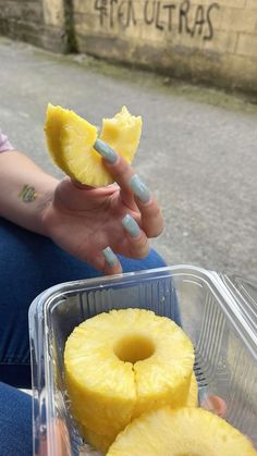 a woman sitting on the ground holding two slices of pineapple in her right hand