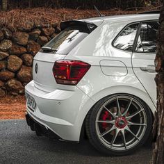 the rear end of a white car parked in front of a pile of rocks and trees