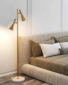 a bed with pillows and a lamp on the floor next to it in front of a white wall