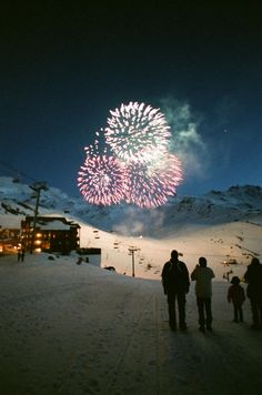 people standing in the snow watching fireworks go off at night with mountains in the background