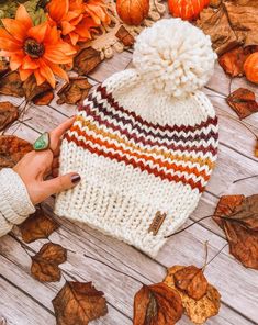 a woman's hand holding onto a knitted hat on top of autumn leaves